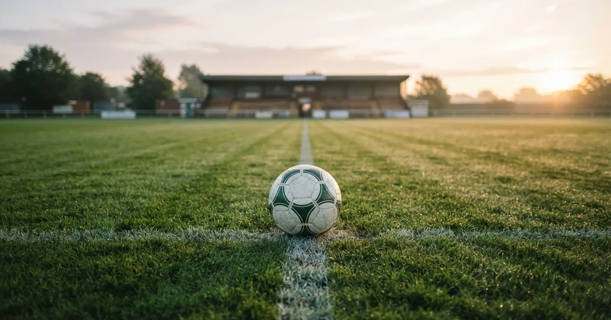 Een voetbal op de middenstip van een grasveld in het ochtendlicht