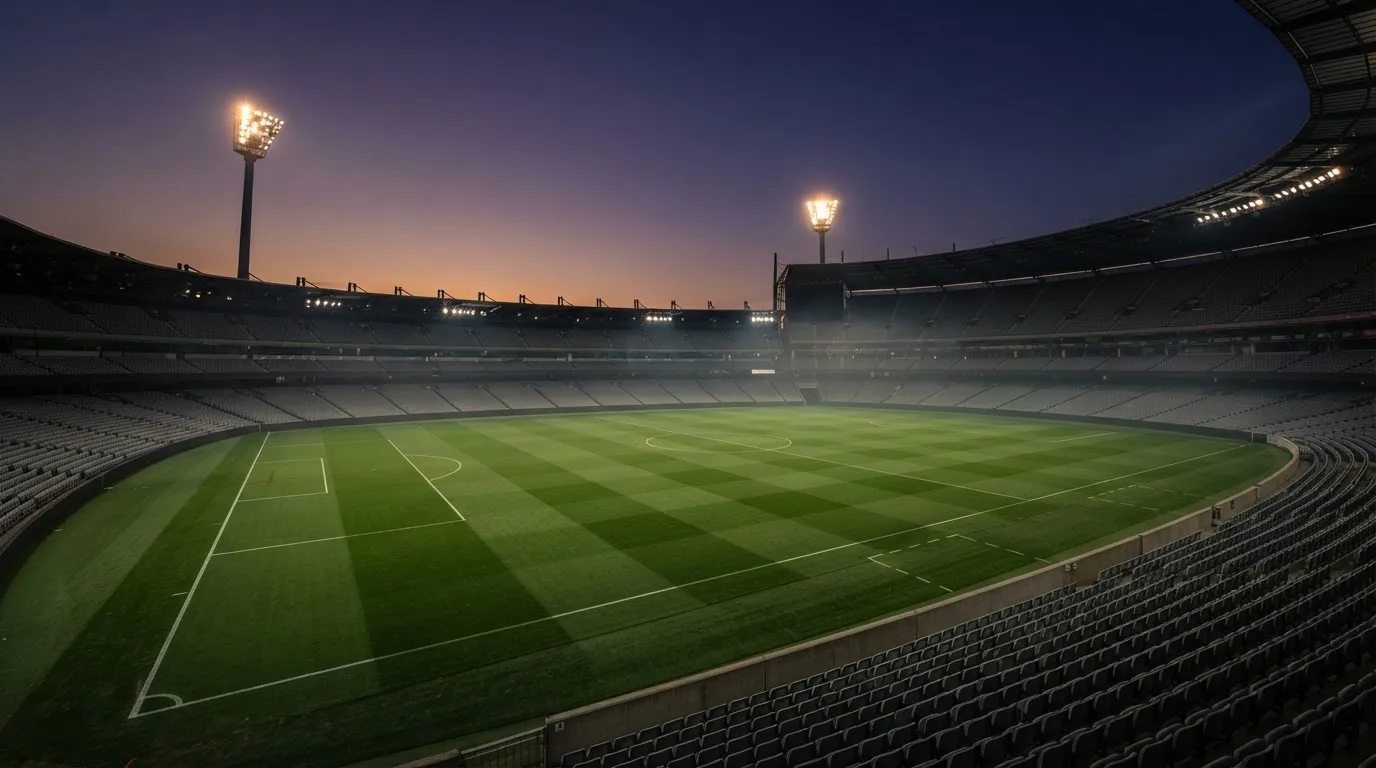 Een leeg voetbalstadion met lichtmasten bij schemering