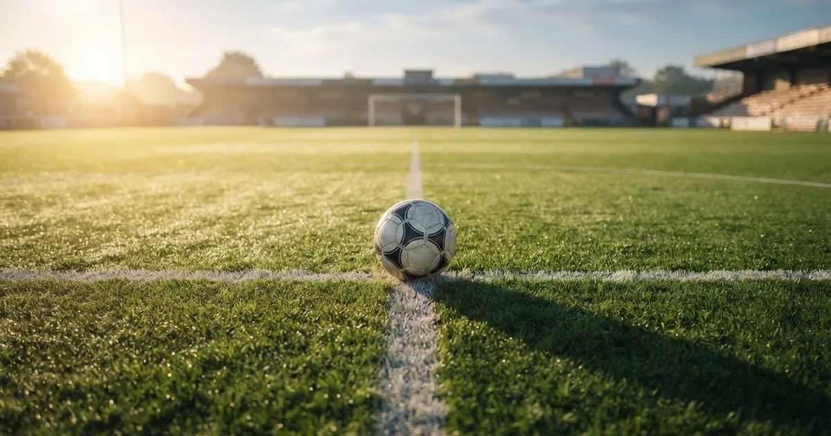 Een voetbal op de middenstip van een grasveld in het ochtendlicht